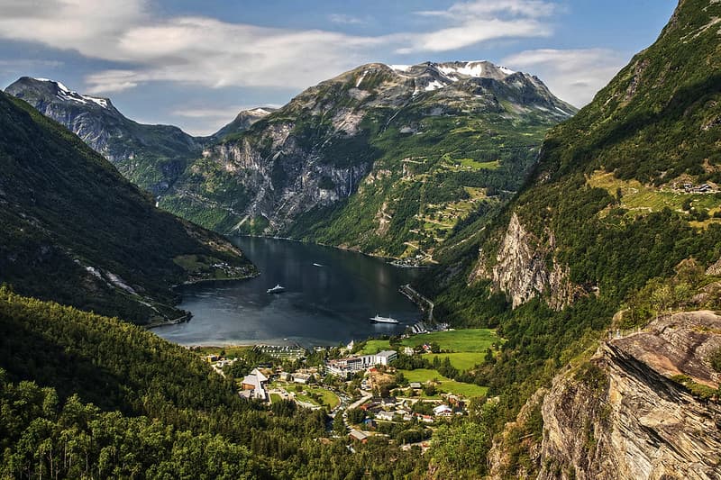 Geirangerfjord with steep green mountainsides dropping into deep blue water, cruise ship in the distance