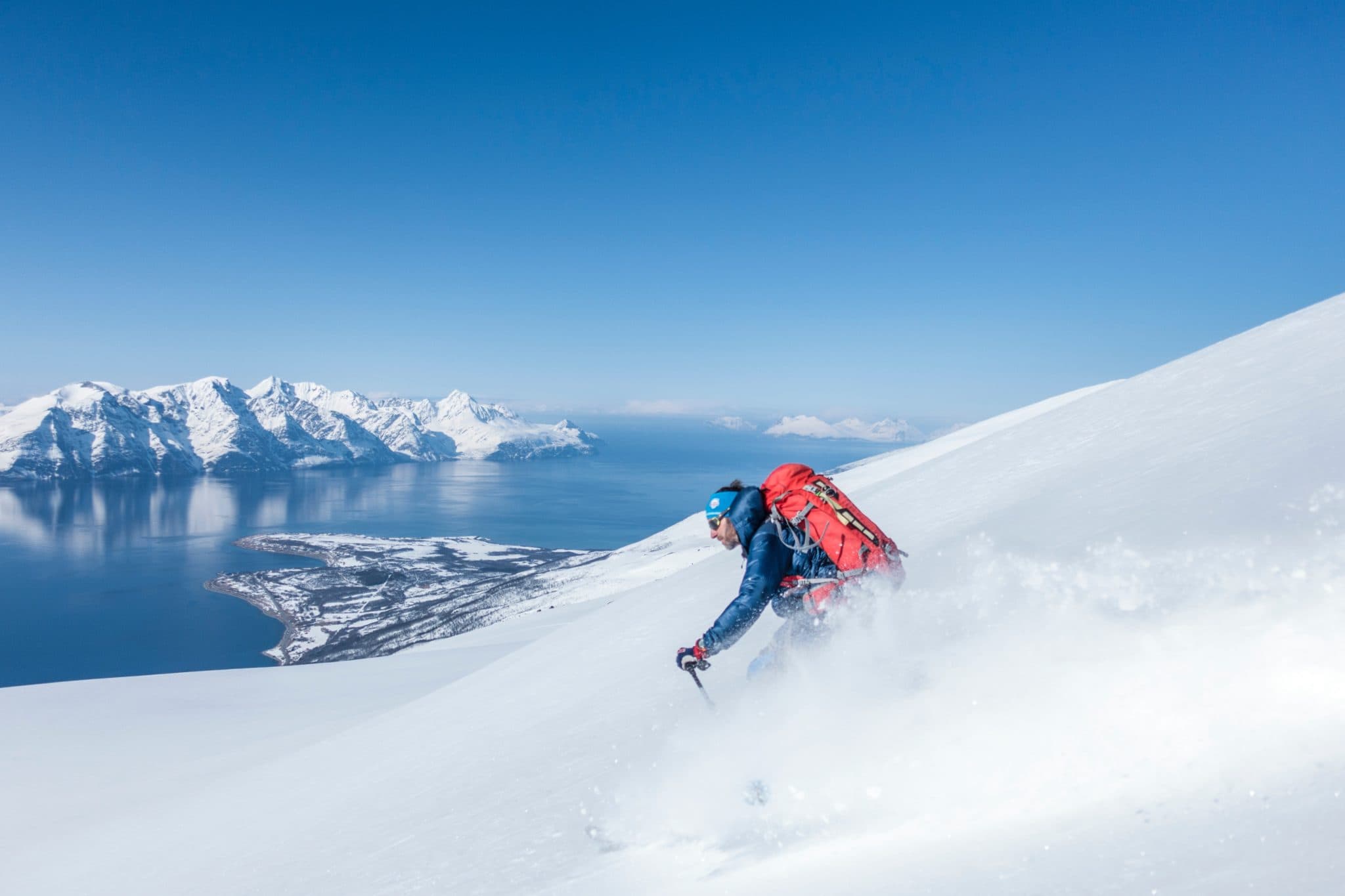 Ski tourer climbing a ridge in the Lyngen Alps with the fjord below